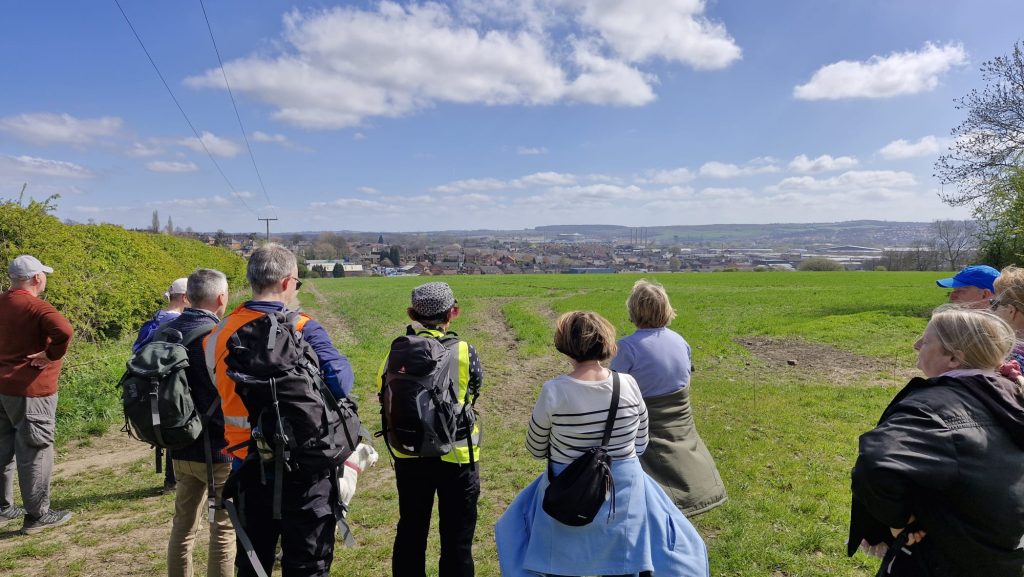 A group of walkers, pray for their local community, standing and looking out over the field to the local village.