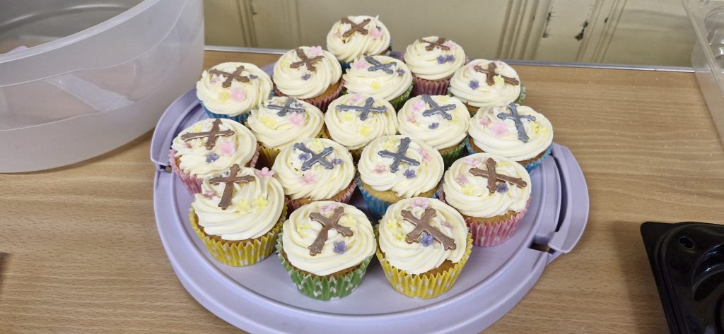 Iced cupcakes with white icing and silver or gold crosses on top.