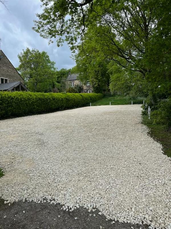 A clear gravel car park, freshly laid. It is surrounded by bushes and trees.