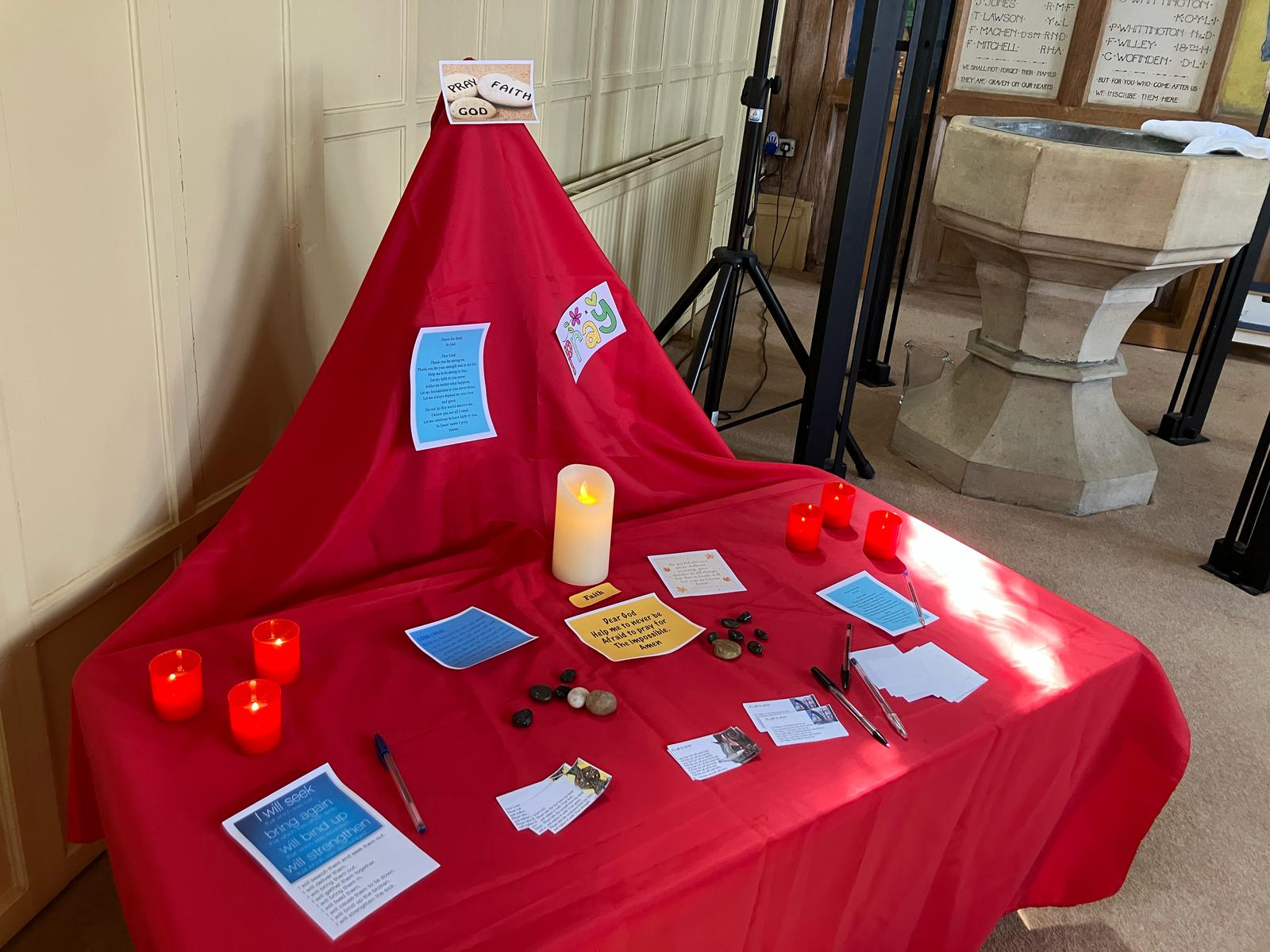 prayer station on a red clothes table. Candles stones and prayer reflections cards are upon it