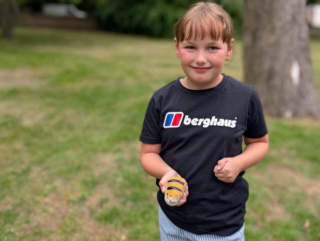 a child holds a rock she has painted to look like a bee