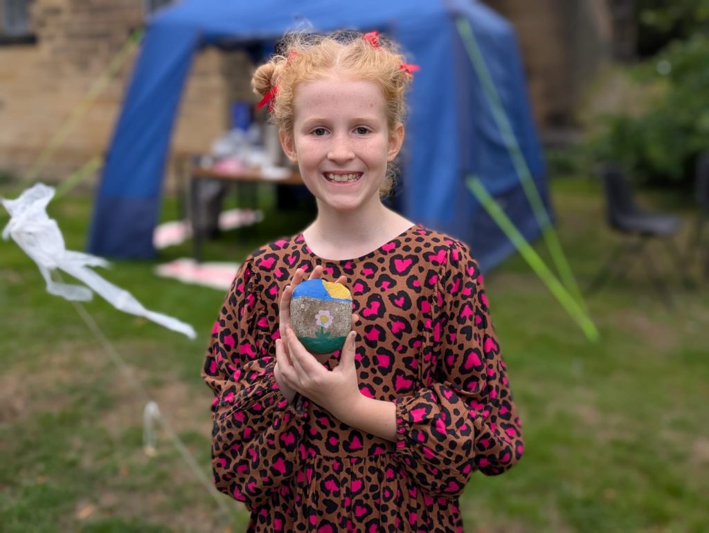 A girl holds a rocks she has painted with a picture of a flower.
