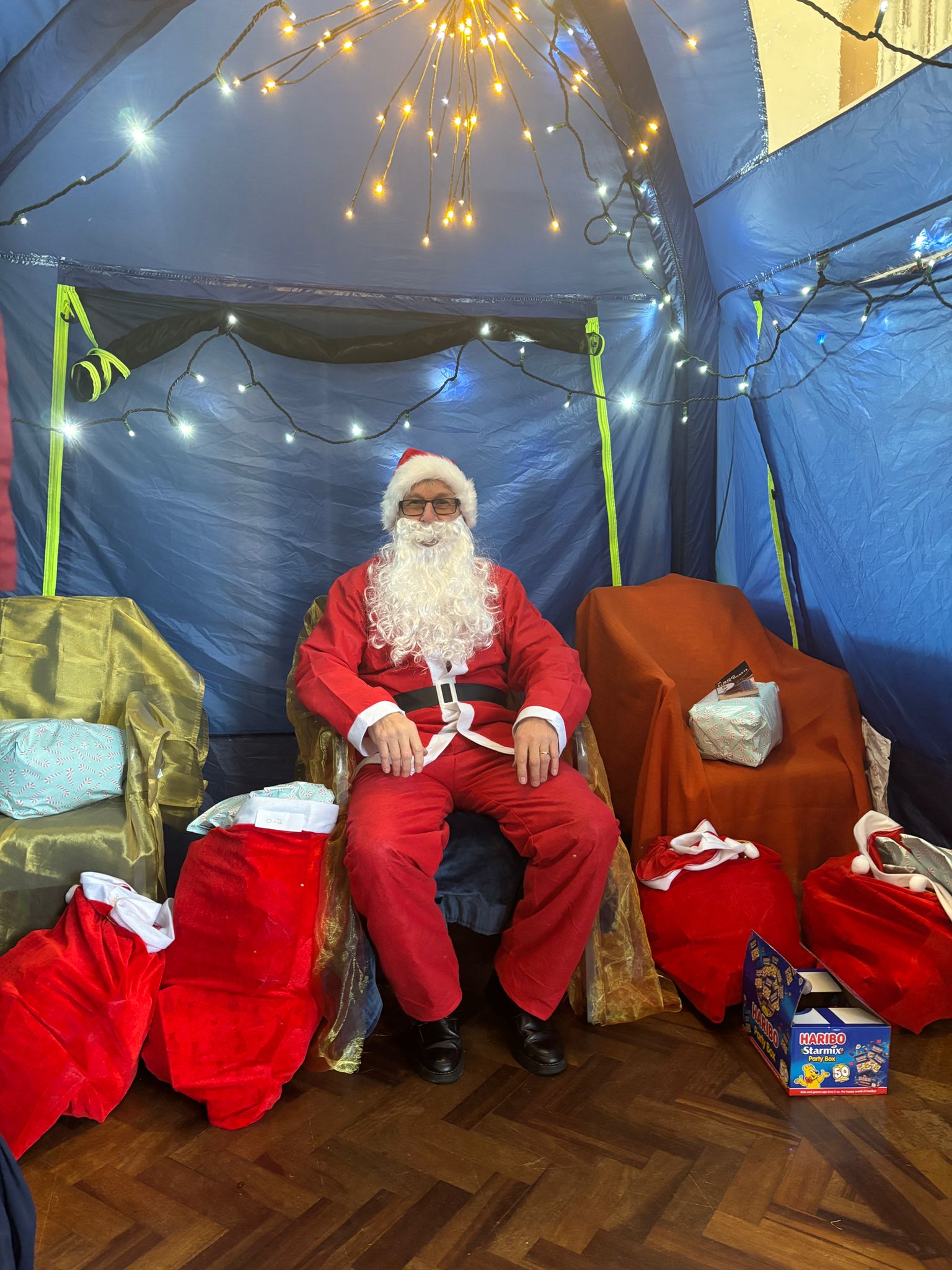 Santa sat inside a blue grotto with sacks of presents in reds and greens surrounding him